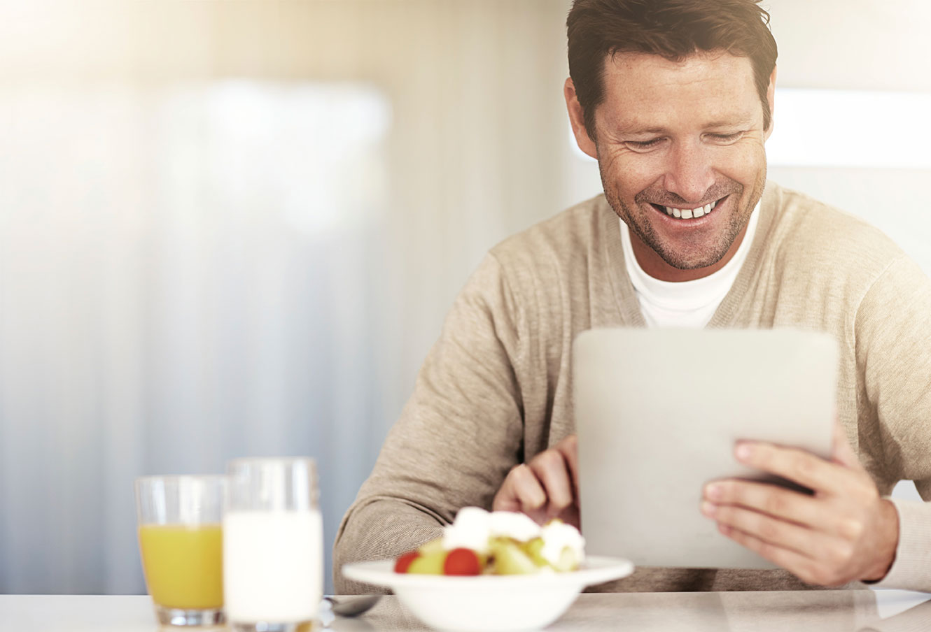 Photo of a man having breakfast, while using a tablet to access online banking.