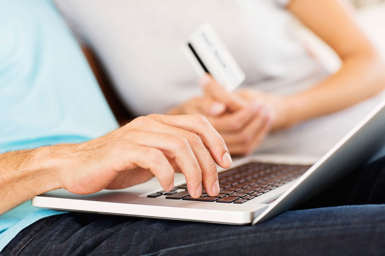Photo of a couple using a laptop and a debit card to make a purchase online.